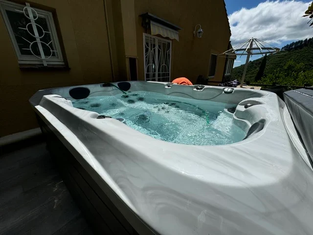 Spa en eau installé sur une terrasse extérieure au pied d’une maison